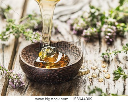 Herbal honey pouring into the wooden bowl. Bowl is on old wooden table surrounded with levender flowers.