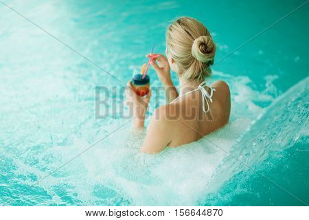 Woman enjoying hydrotherapy and cocktail in spa pool
