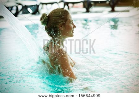 Woman enjoying hydrotherapy and water stream in spa pool