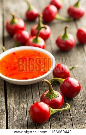 Red chili peppers and chili sauce on old wooden table.