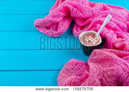 Cozy winter home background cup of hot cocoa with marshmallow old vintage books and warm knitted sweater on white painted wooden board background.