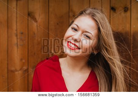 Happy blonde girl with red clothes and lips on a wooden background