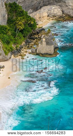 Rock in the ocean with beautiful palms behind at Atuh beach on Nusa Penida island, Indonesia.