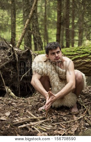 Caveman in animal skin kindles a fire in the forest