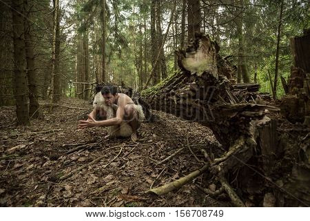 Caveman in animal skin kindles a fire in the forest