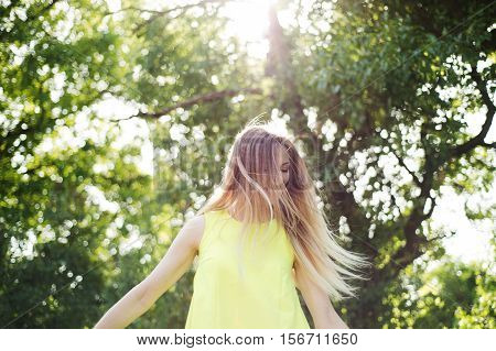 Beautiful young woman with long blowing blonde hair in neon yellow tank top. Sunny summer day.