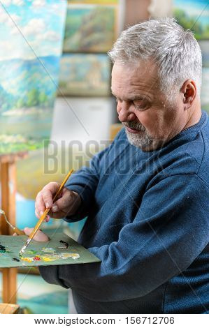 Elderly artist paints a picture oil paints in his studio