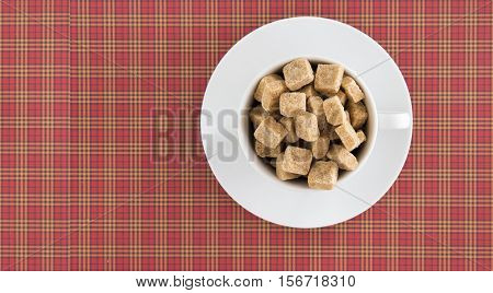 White coffee cup full of brown sugar cubes on red squared background. Top view. Diet unhealty sweet addiction concept