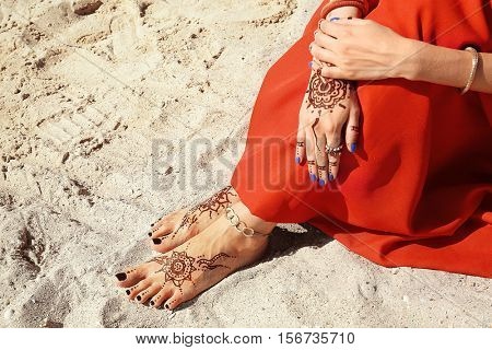 Female legs and hands with henna tattoo on beach sand background