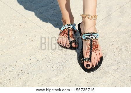 Female legs with henna tattoo on beach sand background