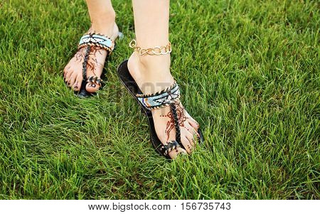 Female legs with henna tattoo on green grass background