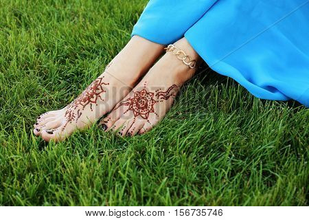 Female legs with henna tattoo on green grass background