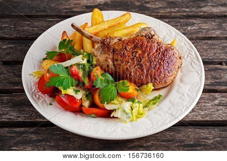 Grilled pork cutlet meat garnished with potato and salad on a wooden table