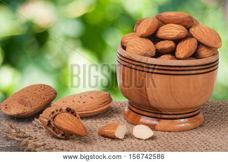almonds in a bowl on the old wooden board with sackcloth and blurred garden background.