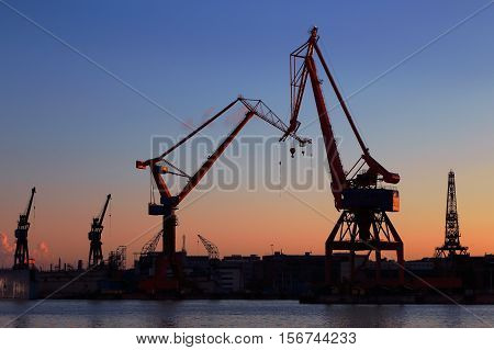Sillouetted cranens in the dockyard during sunset..