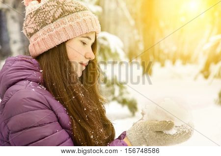 teen pretty girl in winter dawn jacket and knitted pink hat close up portrait on snow park background. handful of snow
