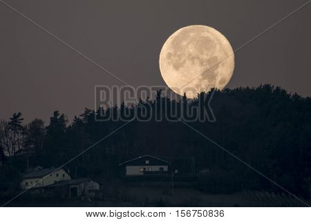 Slovenska Bistrica, Slovenia - November 15 2016: Setting full moon behind hill forest and houses seen on hill. The November supermoon is biggest since 1948 and next is expected in 2034.