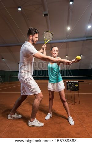 Concentrate on it. Serious professioanl handsome instructor teaching how to serve and play tennis in an indoor tennis court
