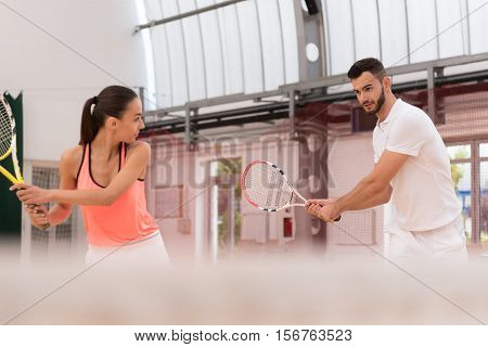 Interesting lesson. Pleasant professional tennis instructor showing young woman how to play tennis while training together