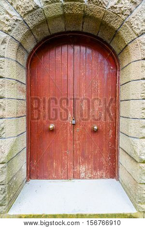Large old red wooden double door in archway