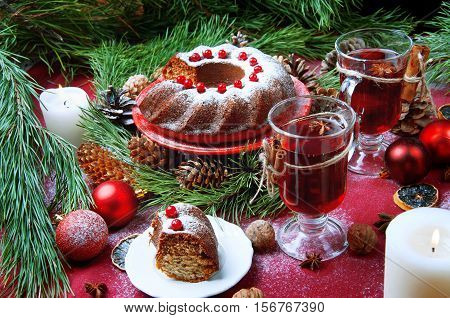Christmas table setting. Bundt cake pudding sprinkled with sugar powder decorated with red currant and mulled wine.