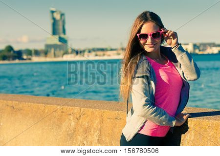 Sport workout fashion concept. Woman wearing sunglasses and tracksuit resting relaxing after doing sports outdoors near sea