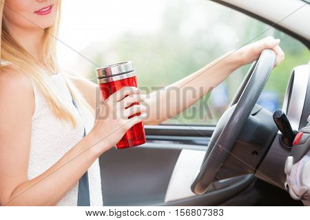 Take an energy boost. Young attractive woman sitting at the wheel drinking hot tea or coffee from vacuum flask thermos while driving the car.