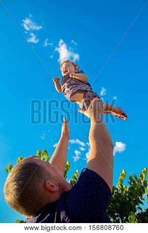 Father throws up and catch the baby. Baby happy and laughing.