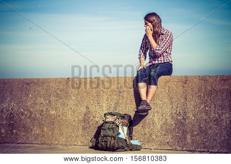 Man tourist backpacker relaxing outdoor sitting on grunge wall against sky. Adventure summer tourism active lifestyle. Young hipster guy tramping