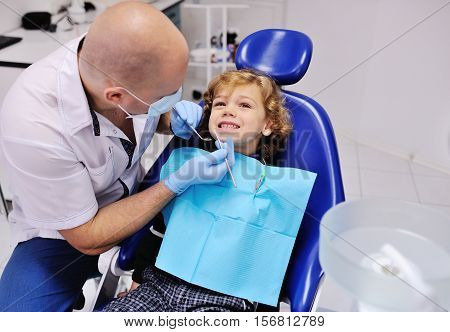 Male dentist examines the teeth of the patient cheerful child with curly red hair. Moloi boy smiling in dentist's chair