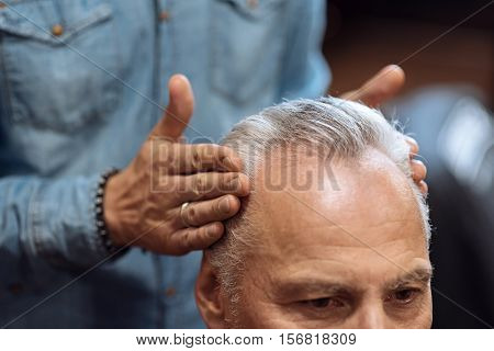 Looking good. Close up of male hairstylist touching senior clients temples while using special hair gel.