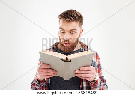 Young beraded man looking in book with eyes wide open over white background