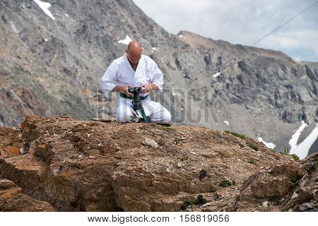 The man in a kimono sits in a lotus position on top of a mountain and watching the pictures in the camera