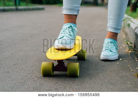 Close-up of female legs in blue jeans and sneakers standing on a yellow skateboard low angle shooting