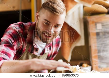 profession, carpentry, woodwork and people concept - carpenter working with wood plank at workshop