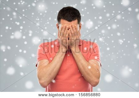 people, fear, emotions, winter and stress concept - man in white t-shirt covering his face with hands over snow on gray background