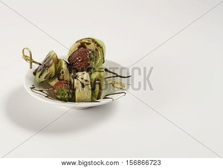 Skewers of strawberries bananas and kiwis on a small plate with a white background.