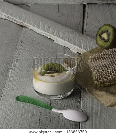 Two glasses with greek yogurt with kiwi and honey with a piece of bee panel and half a kiwi on a wooden board.