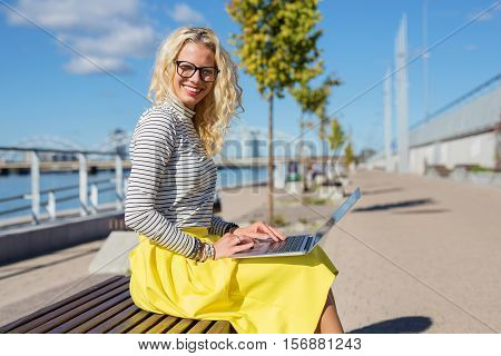 Stylish woman sitting ouside and working on laptop