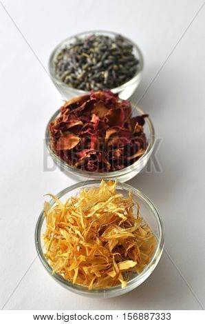 Dried marigold (calendula) petals with lavender and rose for beauty treatments in clear glass bowls - top view with copy space