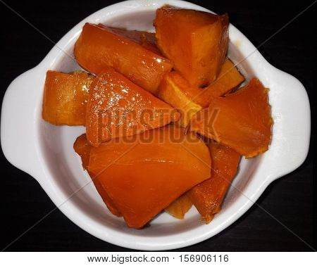 Slices of pumpkin with sugar baked in the oven. The white plate on a black background