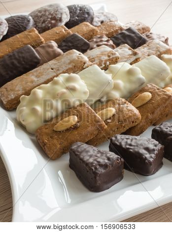 Closeup of an assortment of typical German Gingerbreads such as Lebkuchen Aachener Printen and Spitzkuchen arranged on a large white porcelain serving plate. Selective Focus. Shallow Depth of Field.