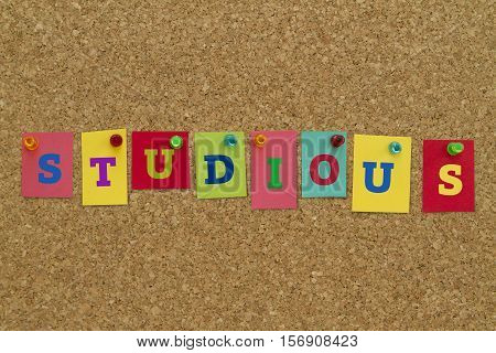 Studious word written on colorful sticky notes pinned on cork board.