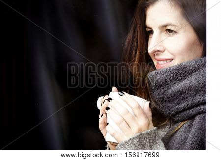 attractive adult woman drinking coffee and looking out of the window on cold day, close up portre in winter time