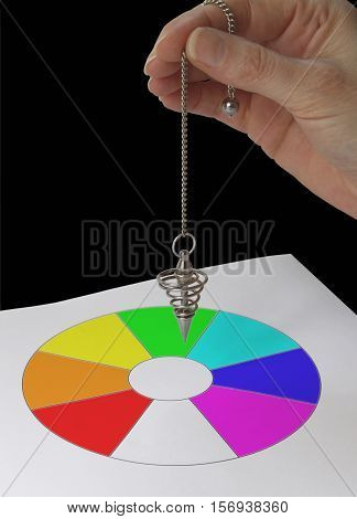 Radionics practitioner with Color Dowsing chart - female hand holding a spiral dowsing pendulum over a color filled circular sectioned dowsing chart on a black background