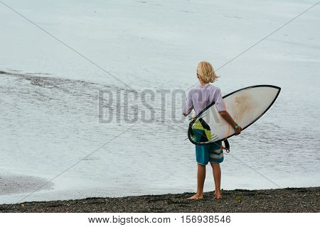 Young surfer holding his surfboard. On his back.
