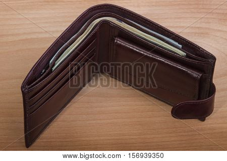 brown leather men's wallet with money on a wooden background