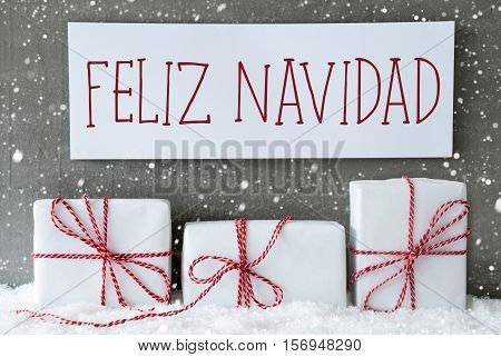 Label With Spanish Text Feliz Navidad Means Merry Christmas. Three Christmas Gifts Or Presents On Snow. Cement Wall As Background With Snowflakes. Modern And Urban Style.