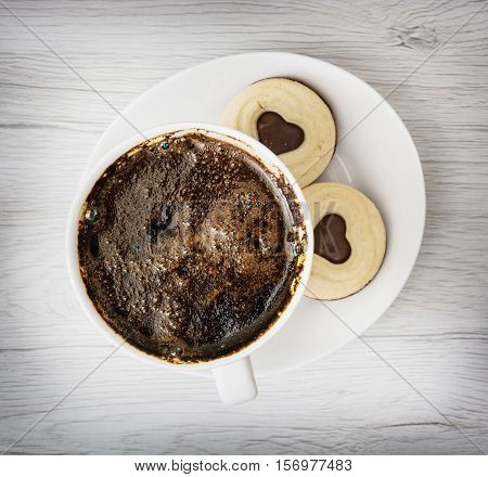 Cup of black coffee with two jam biscuits in the shape of heart on the wooden background. Food and drink. Sweet delight.