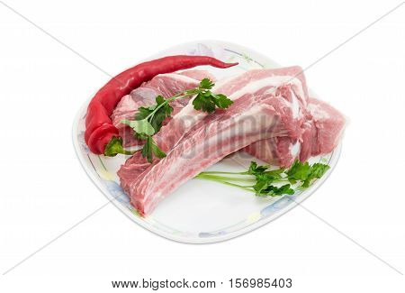 Two pieces of uncooked fresh pork belly with ribs chili pepper and twigs of parsley on a dish on a light background